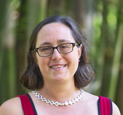 Rachel Prunier smiling at the camera while standing in front of a blurred, green, woodsy background